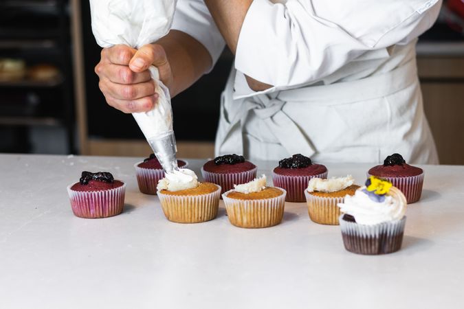 Crop cook decorating cupcakes with whipped cream