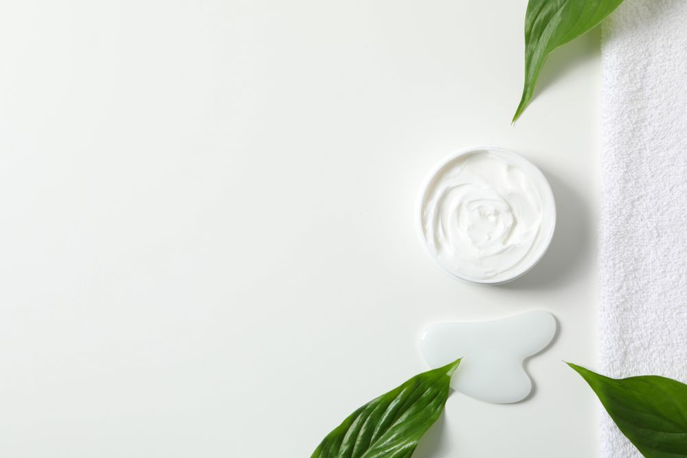 Jar with cream, towel and gua sha on light background, space for text