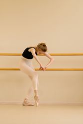 Ballet dancer stretching, leaning forward and holding onto the barre.