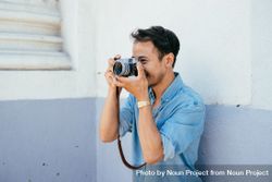 Man in blue shirt holding camera to his face smiling and taking photos 0yXLqb