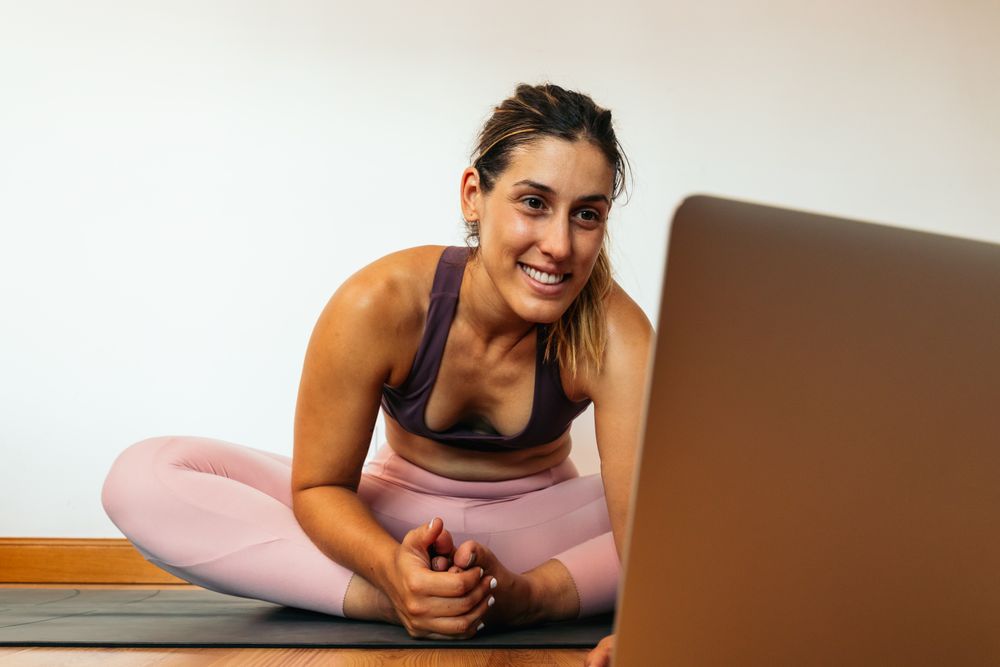 Woman in sportswear doing yoga with laptop at home