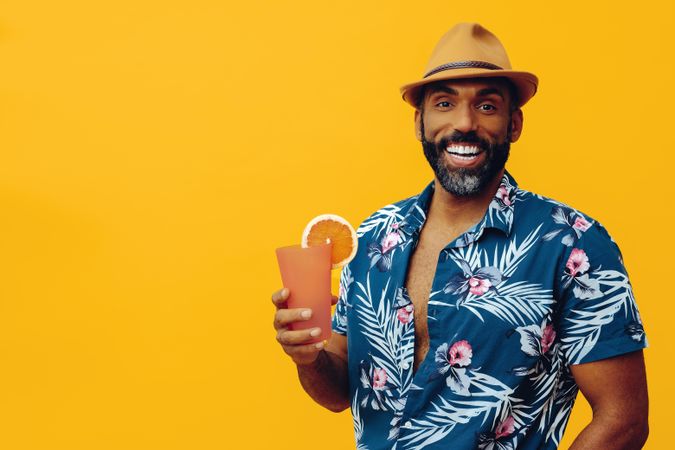 Smiling male holding a drink while wearing colorful shirt with yellow background, copy space