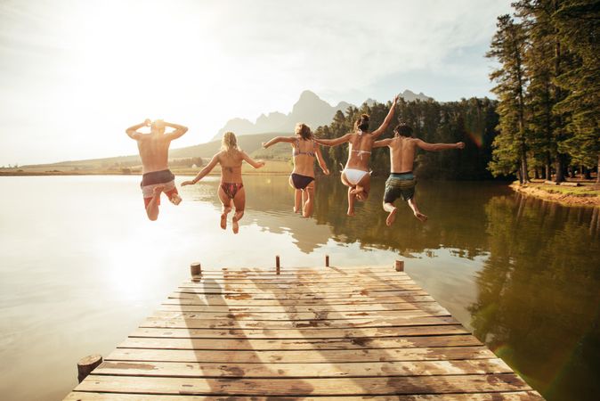 Portrait of young people jumping from pier into lake together