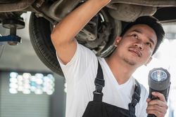 Close up of male auto repairman working on undercarriage of vehicle