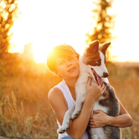 Whimsical woman holding her husky dog in field at dusk