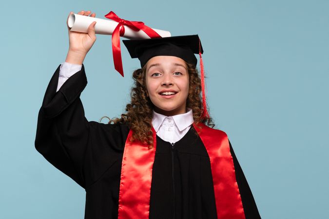 Young girl in graduation gown holding diploma above her head and smiling.