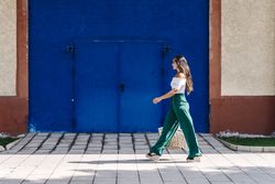 Young happy trendy woman walking in city against blue door