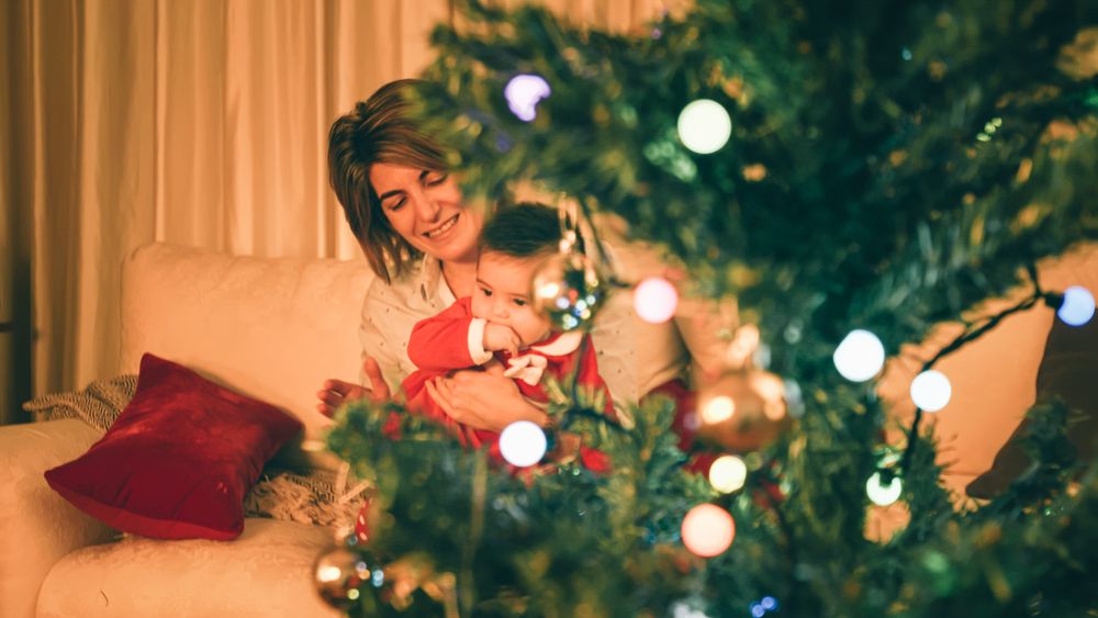 Mother playing with baby near Christmas tree