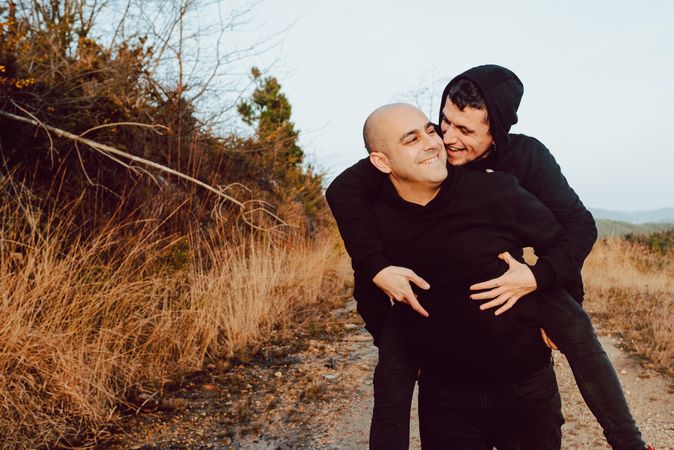 Smiling man holding on back cheerful guy on road on hill