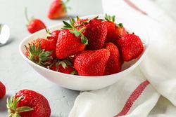 Plate with fresh strawberries, spoon and kitchen towel on bright background, closeup and space for text