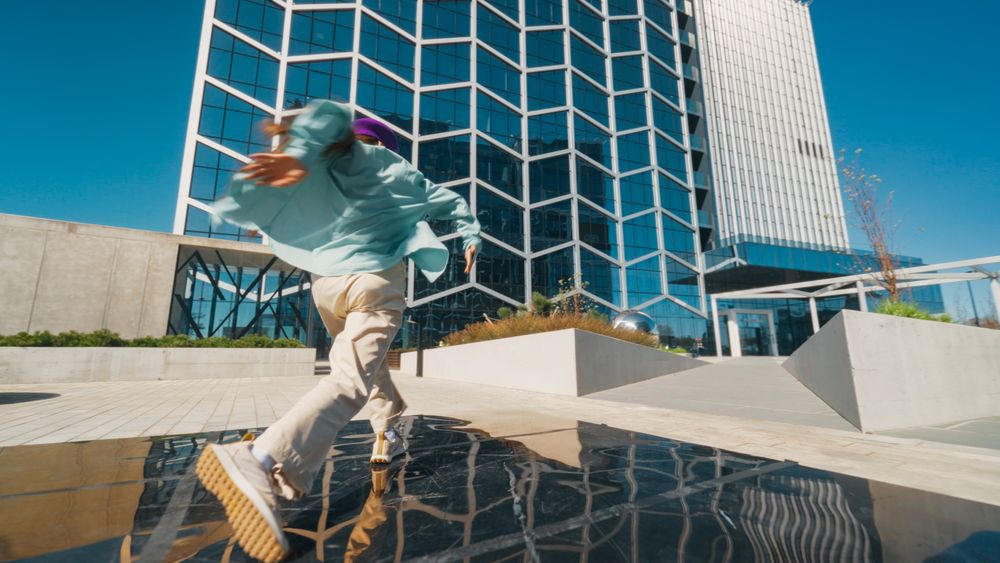 Dynamic Image Of A Young Person Energetically Breakdancing In A Modern Plaza,