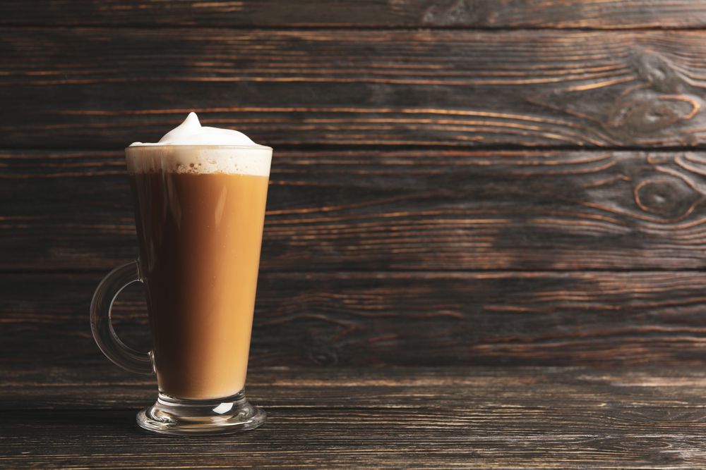 Glass cup of latte on wooden background, space for text