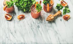 Cold Moscow mules with blood oranges and citrus reamer on marble table