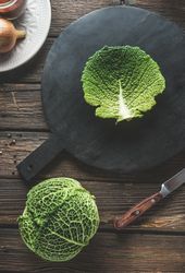 Whole raw savoy cabbage and cabbage leaf on cutting board on rustic wooden kitchen table with knife.