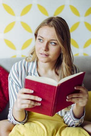 Young happy female reading book on sofa