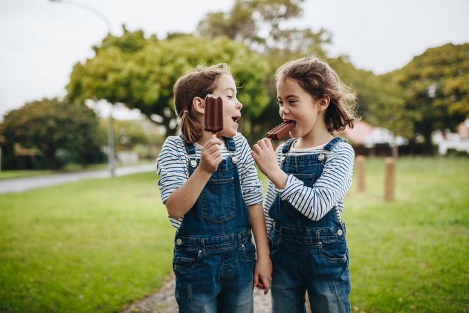 Two little girls enjoying eating candy ice cream outdoors