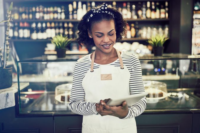Woman in apron taking orders with tablet in modern bistro