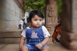 Girl in blue denim dungaree sitting on concrete floor outdoor