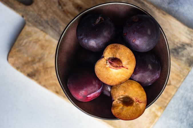Bowl of halved ripe plums on wooden cutting board