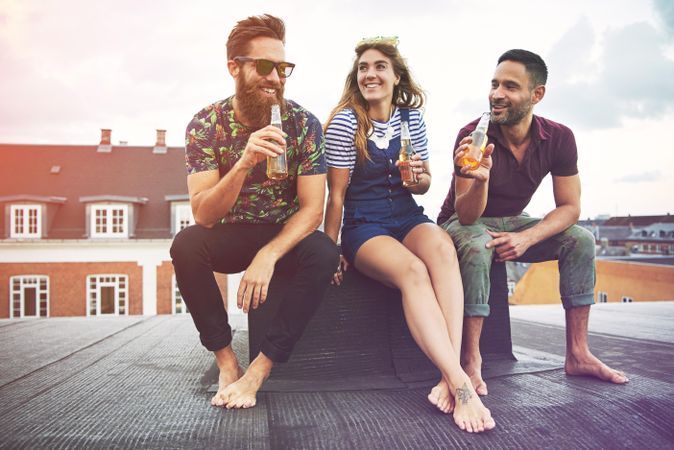 Three friends relaxing outside on a rooftop with beer