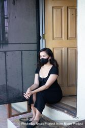 Beautiful woman with mask sitting on front steps of house looking out 4NE6l5