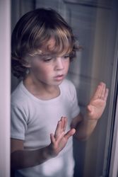 Attentive little child looking out window through glass