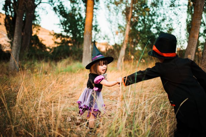 Little girl in witch costume reaching out to her brother in the forest