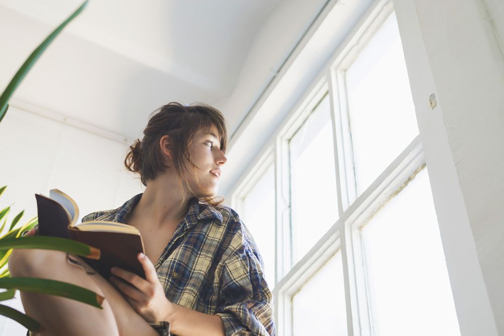 Female in flannel shirt writing in notebook looking out of window