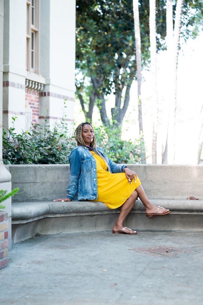 Full length shot of woman sitting on stone bench in front of old brick building