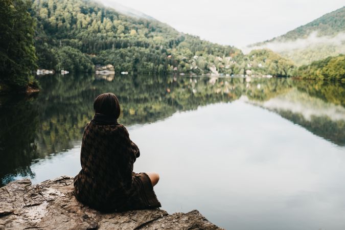 Woman sitting with blanket near lake and mountains