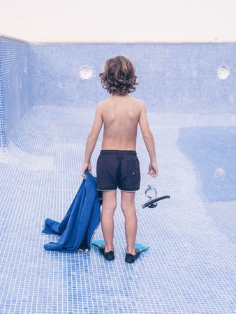 Preteen boy in flippers with diving mask on empty pool