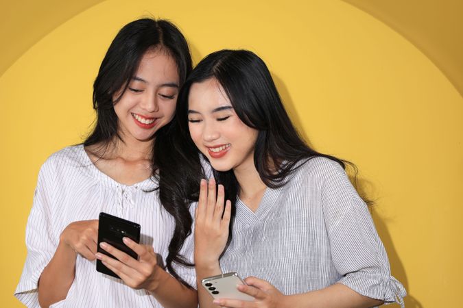 Cheerful Asian Young Woman Showing Some Funny Video Meme to Her Female Friend
