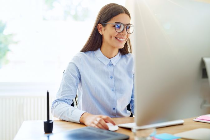 Happy woman in blue shirt working from monitor in her bright office