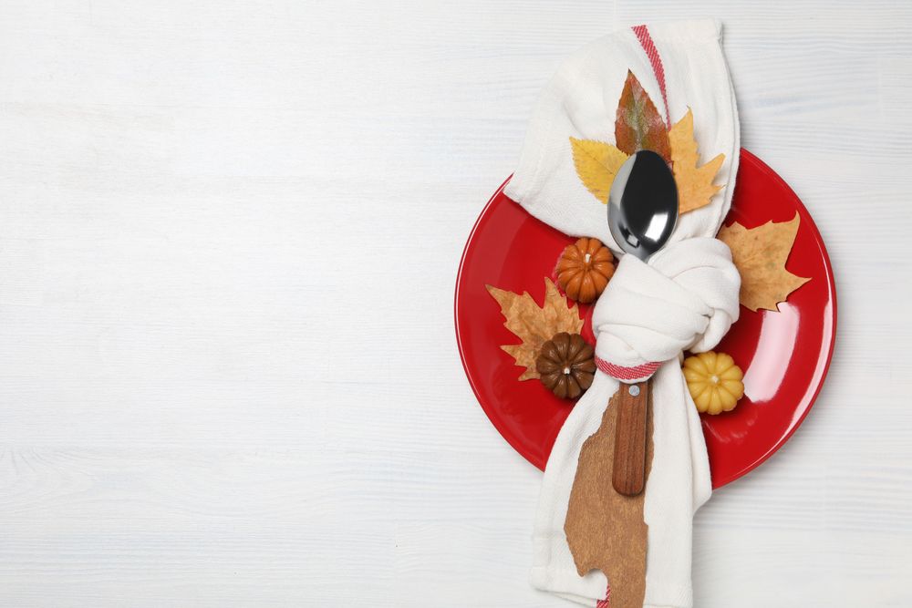 Spoon in towel on plate, leaves and pumpkins on light background, space for text
