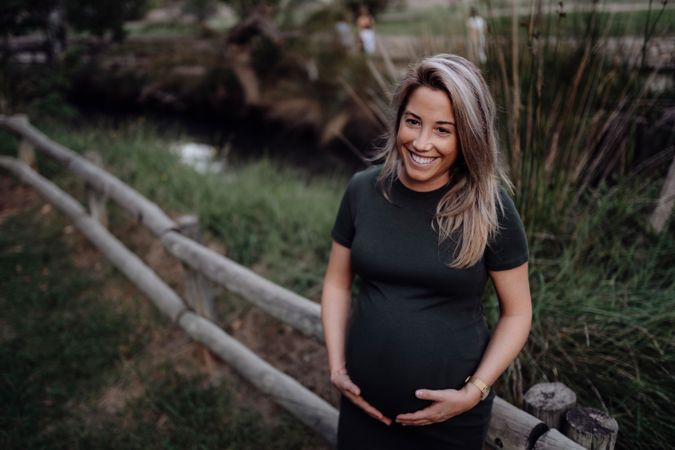Happy pregnant woman standing at river in park