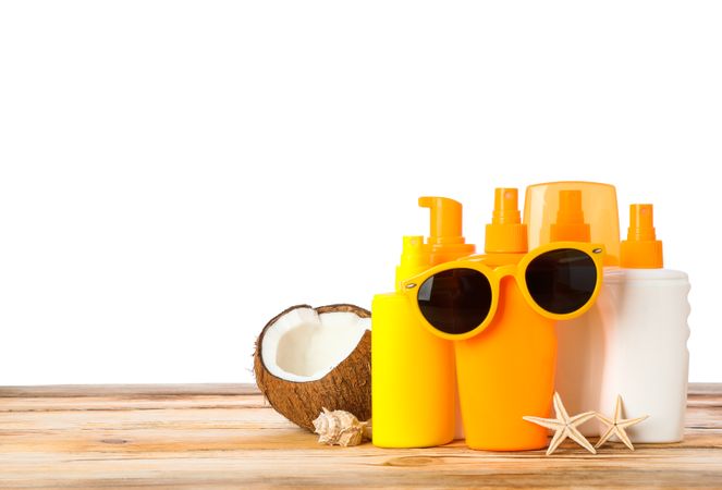 Sunscreen sprays with starfishes, coconut and sunglasses on wooden table isolated on neutral background. Safe tan