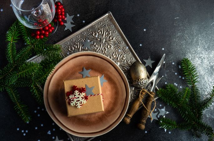 Rustic plate with gift box, cutlery and glass surrounded by wintry pine and ornaments