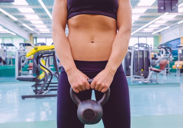 Torso of fit woman holding kettle bell in gym