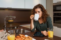 Woman sipping coffee over tablet screen at breakfast