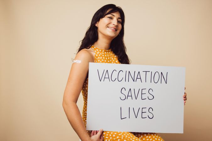 Beautiful woman holding a signboard with "vaccination saves lives" written on it