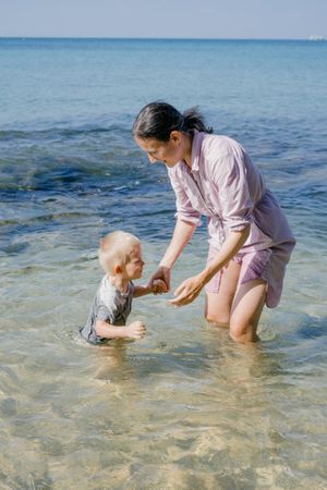Woman and small kid having fun with water while relaxing on seacoast at resort