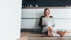 Woman with laptop sitting on the kitchen floor wearing earphones 49Ky60