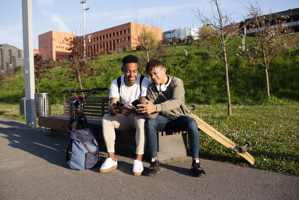 Young Black men sitting on bench with smartphone