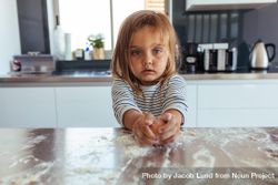 Little girl breaks an egg with flour on the kitchen counter 4OYJg0