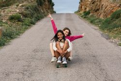 Happy diverse women riding longboard on road