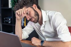 Stressed young man feeling burnout while working on a laptop.