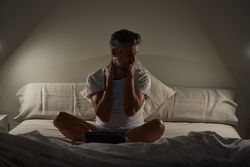 Exhausted mature ethnic man resting after working on tablet in bed