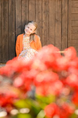 Content girl resting against wooden wall in daylight