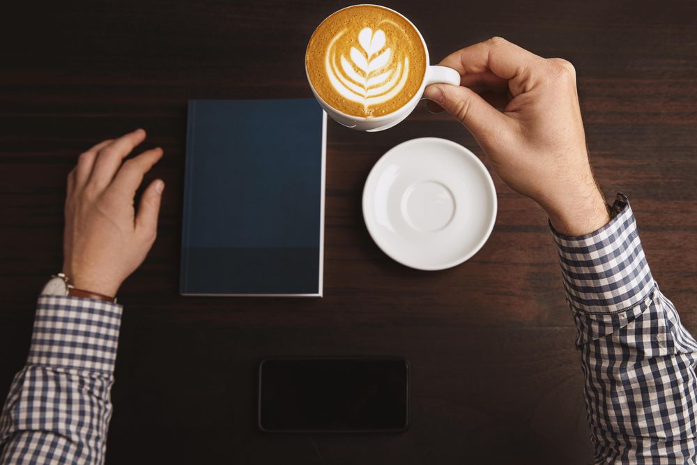 Top view of man in plaid with cappuccino and closed notebook