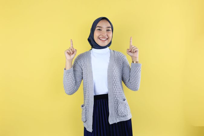 Asian Young Muslim Woman Wear Hijab Headscarf Smiling and Pointing Finger Above